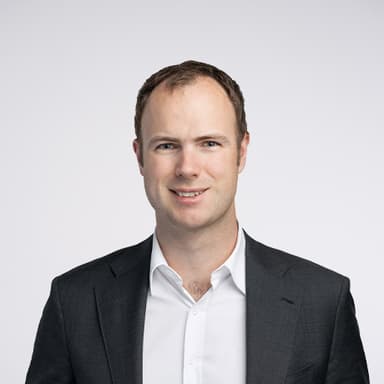 Professional headshot of Julian Granger-Bevan in a dark suit jacket and white shirt against a light gray background.